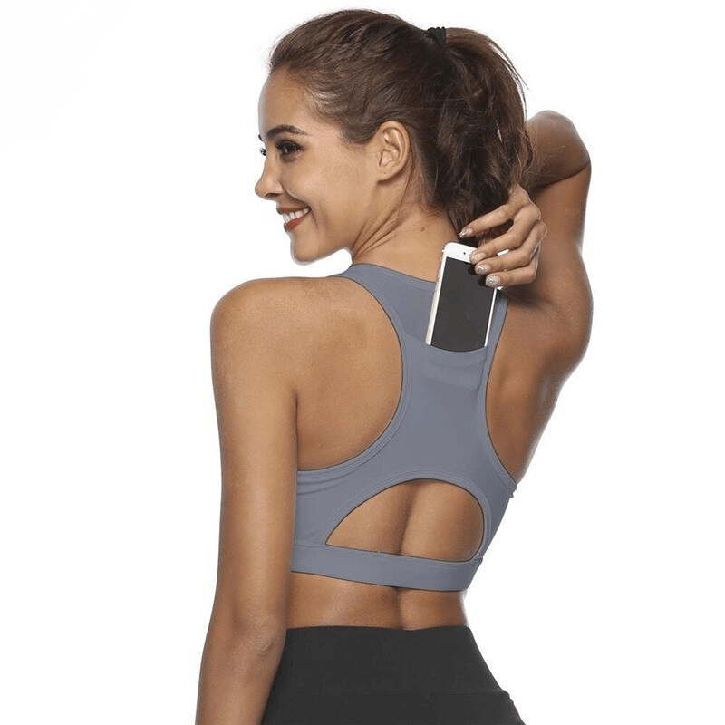 Woman wearing stylish elastic sports bra with back pocket, inserting phone, ideal for fitness and workouts.